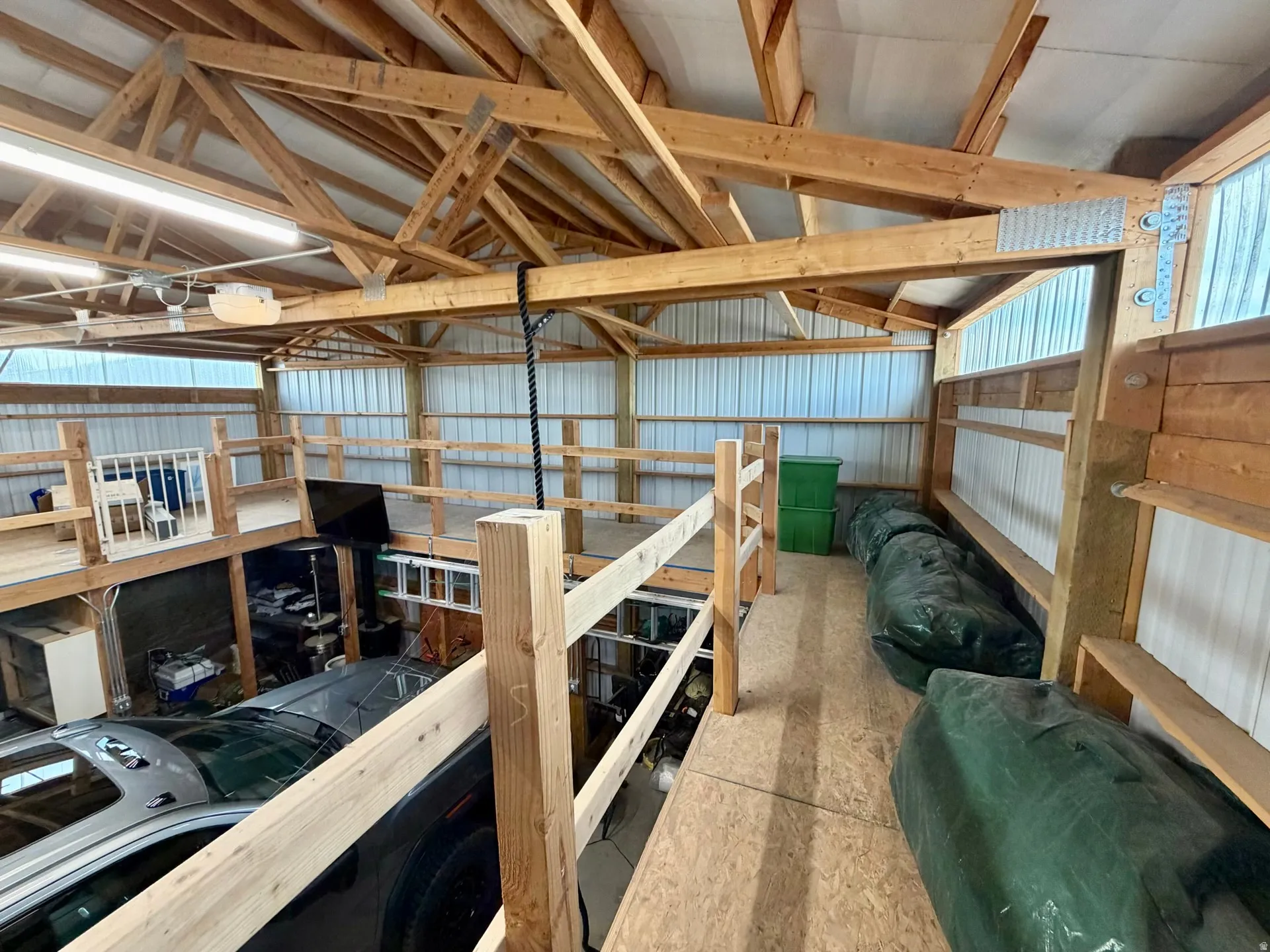 Expansive multi-level interior featuring exposed wood beams and trusses, corrugated metal wall panels, and an open upper loft area with wood railing