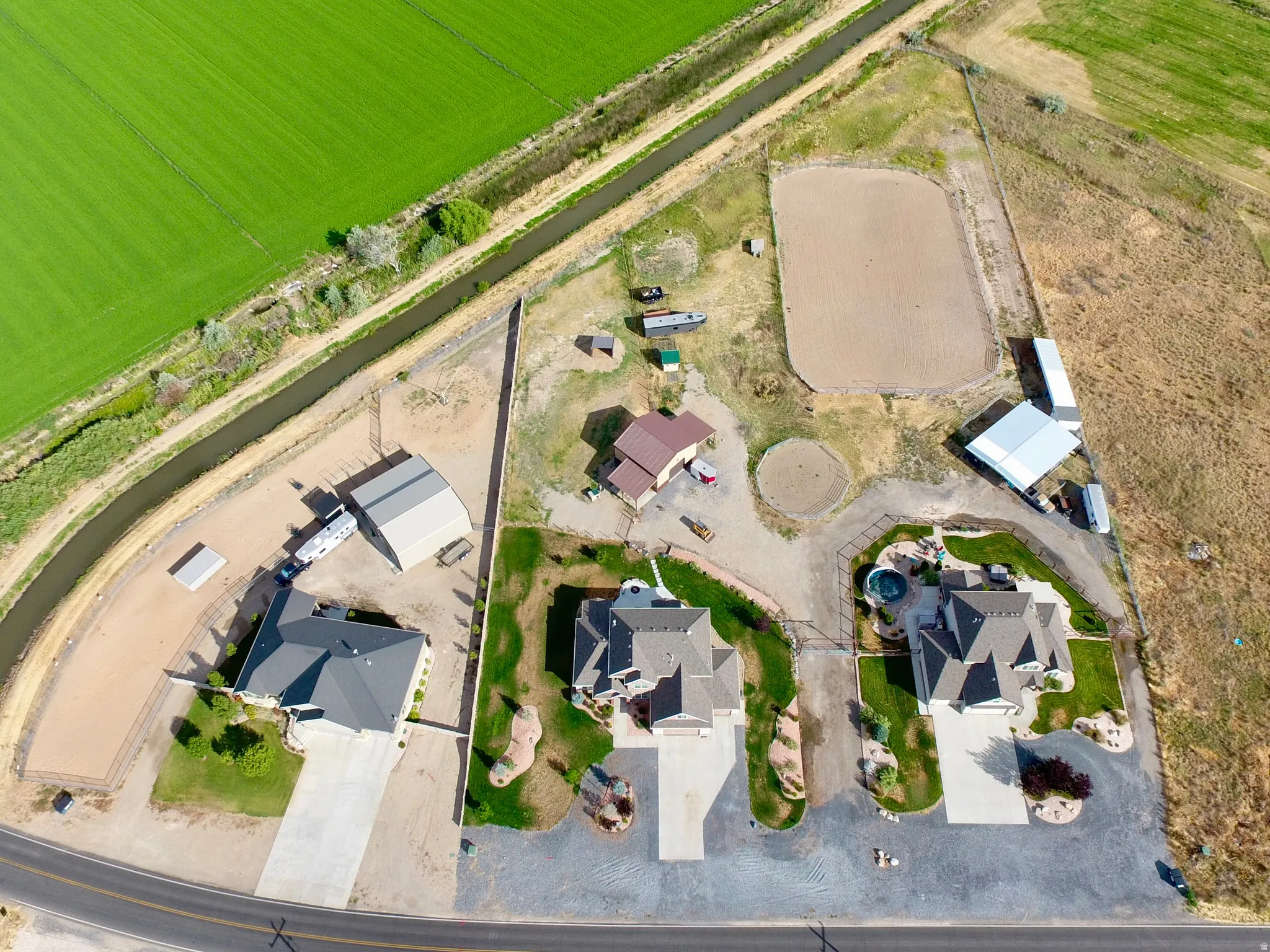 Aerial perspective of a multi-structure property featuring a main residence with an attached garage, a secondary residence, and a third residence