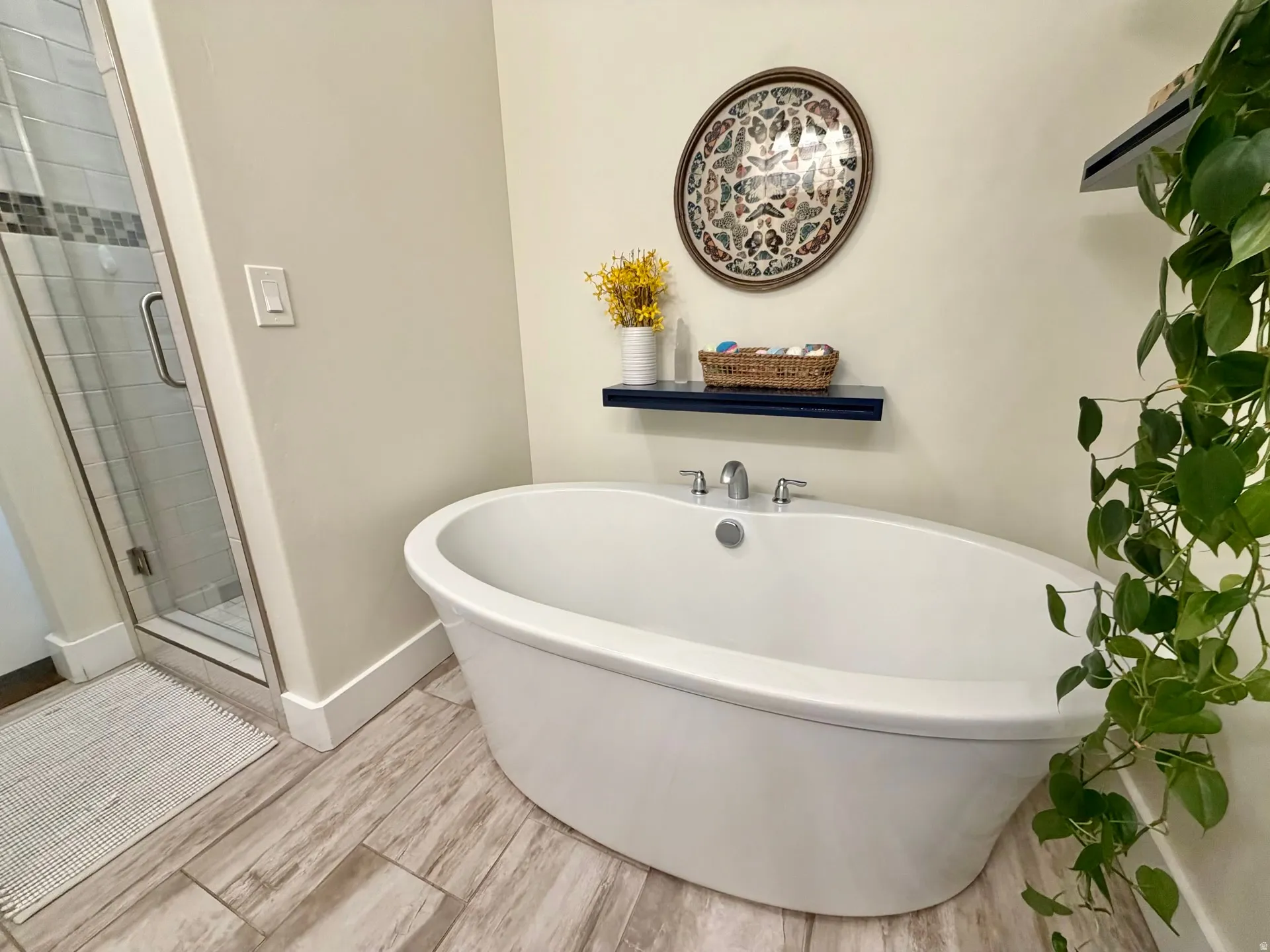 Freestanding soaking tub with chrome fixtures and wood-finish tile flooring