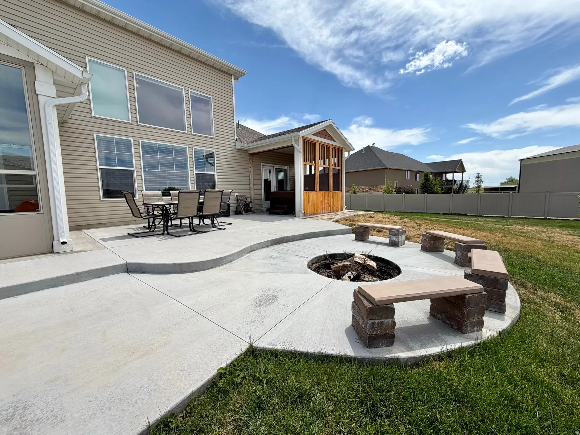 Expansive concrete patio area featuring a built-in fire pit with stone block seating, a screened-in porch with wood paneling, and a vinyl-sided exterior with multiple windows
