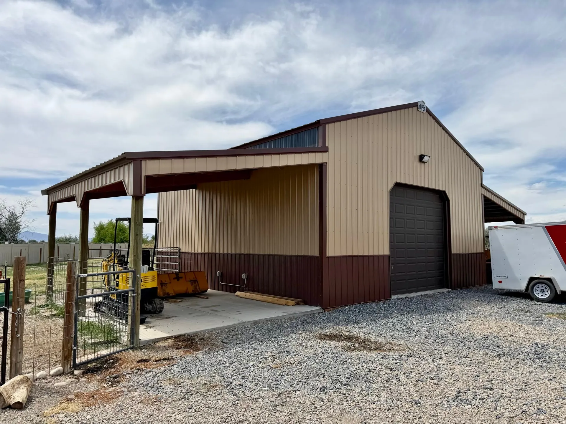 Two-tone metal building featuring a prominent brown roll-up door, covered concrete pad, and covered side porch