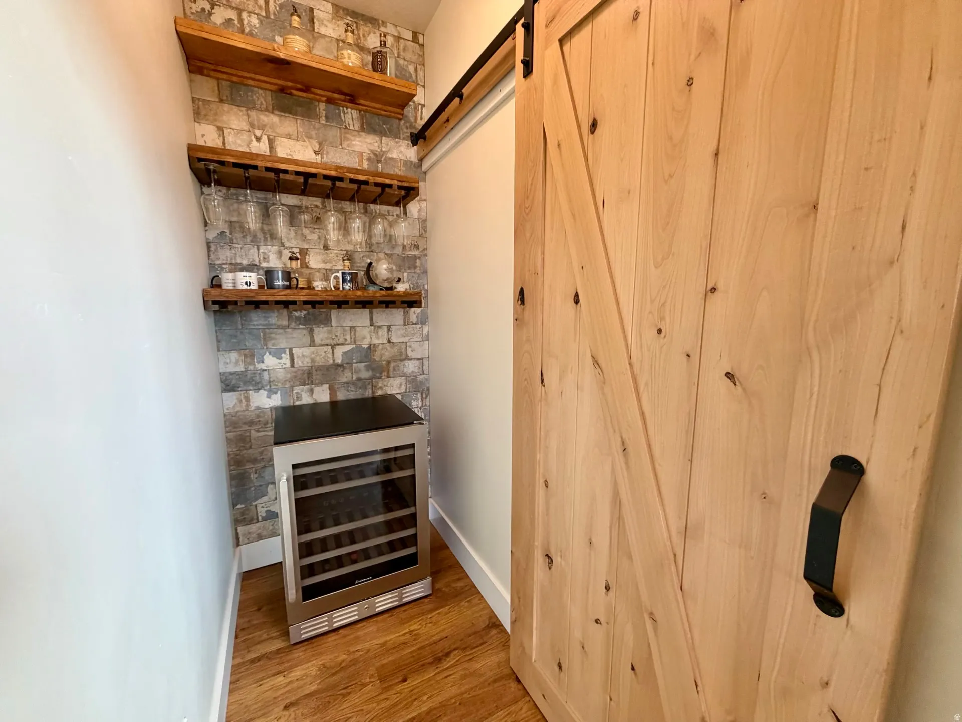 Dedicated beverage station featuring a brick-finish accent wall with three wood-finish shelves, a built-in wine rack, and a stainless steel beverage refrigerator