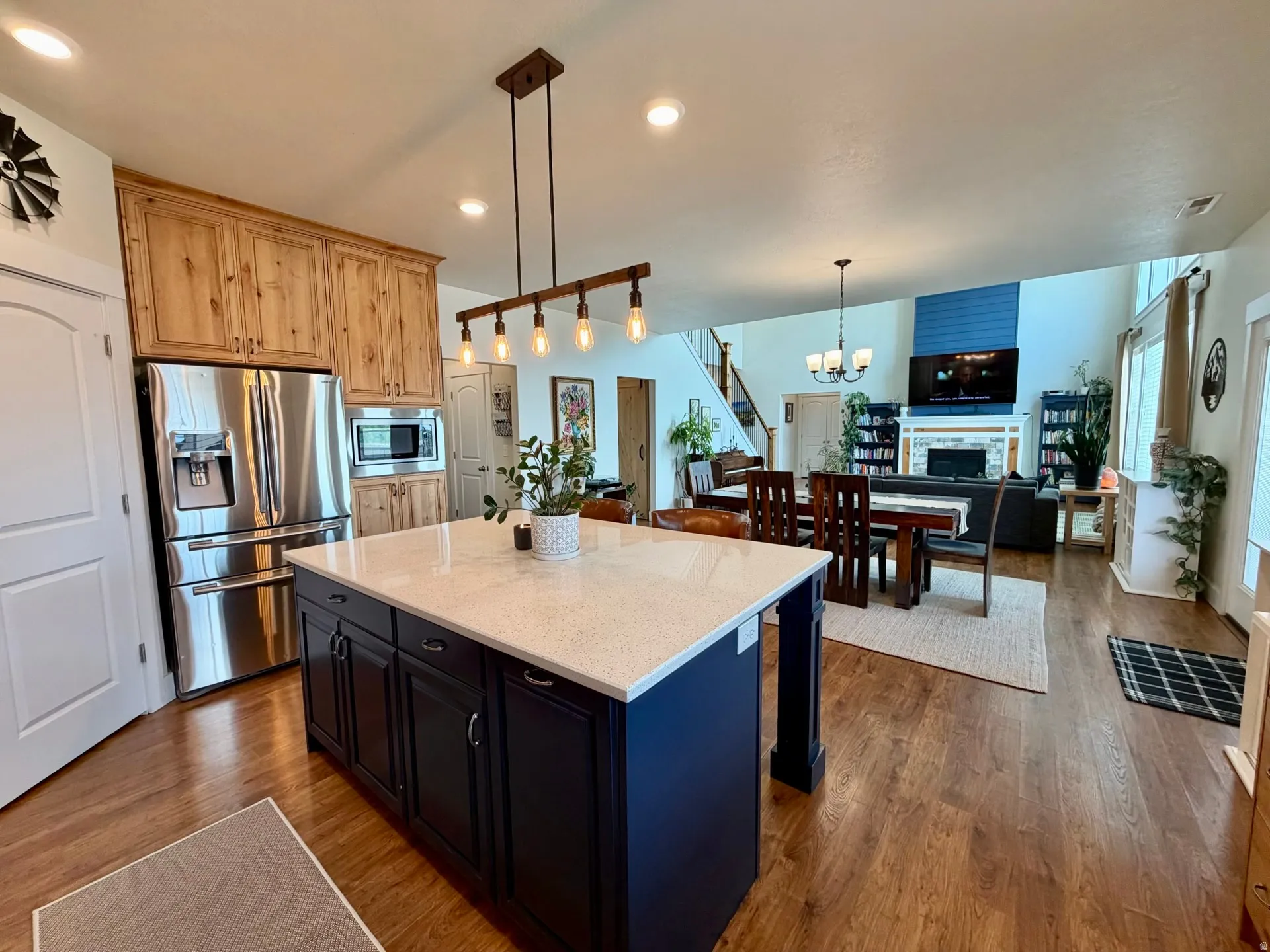 Spacious open-concept interior featuring wood-finish flooring, a kitchen island with a light-colored countertop, stainless steel appliances, and a living area with a fireplace