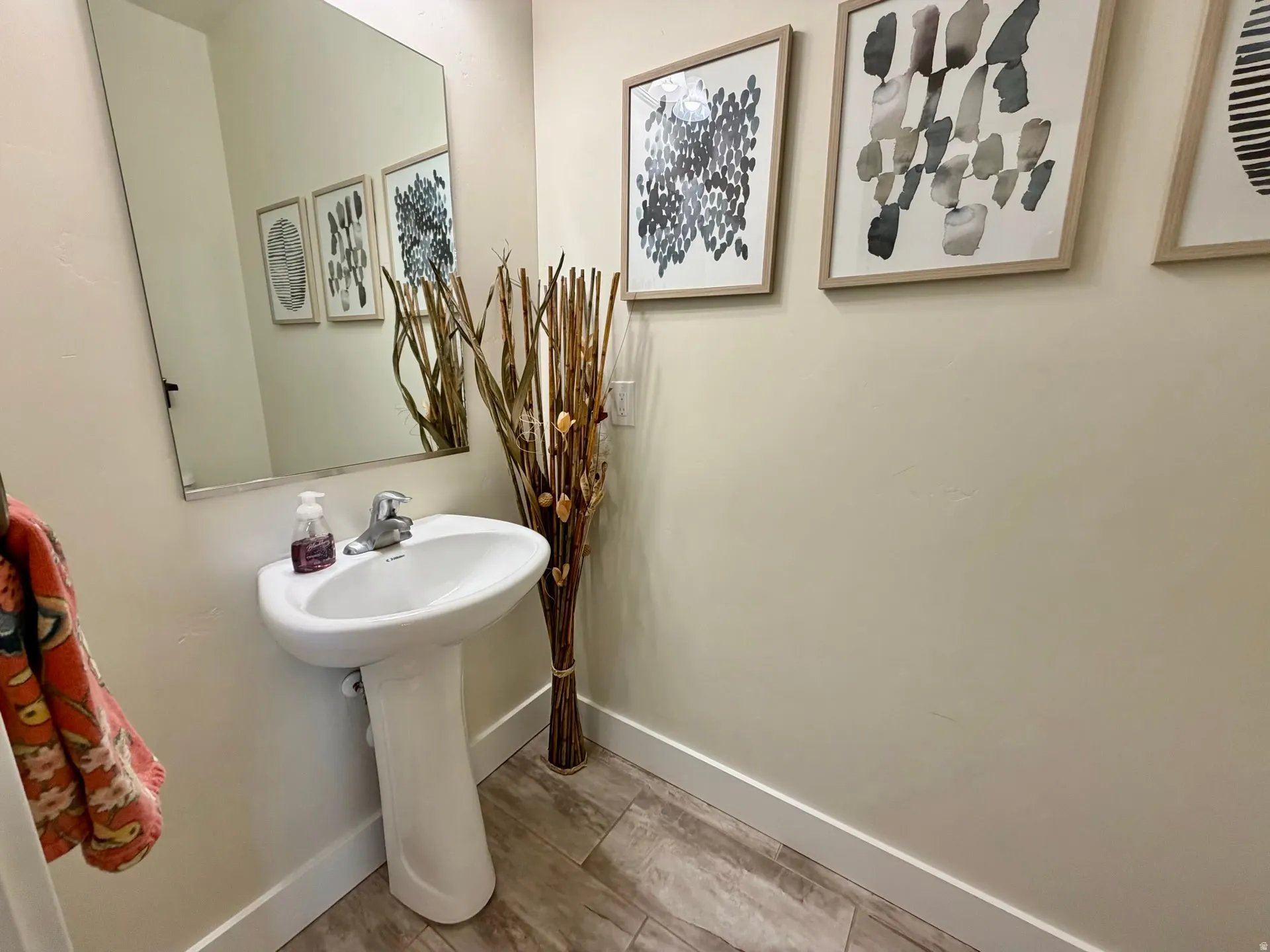 Pedestal sink with chrome faucet, large wall-mounted mirror, light-colored walls, and wood-finish tile flooring