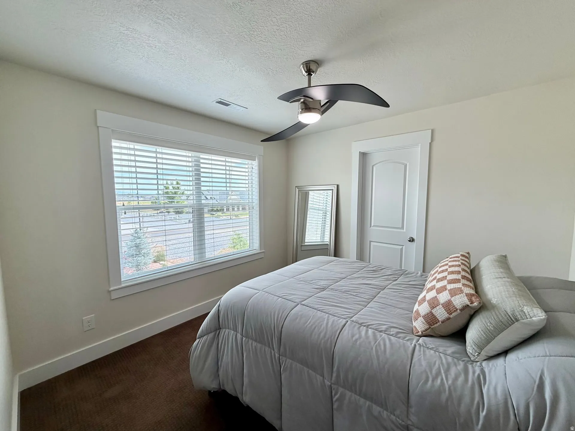 Room featuring a large window with white blinds, dark brown carpeting, and light-colored walls