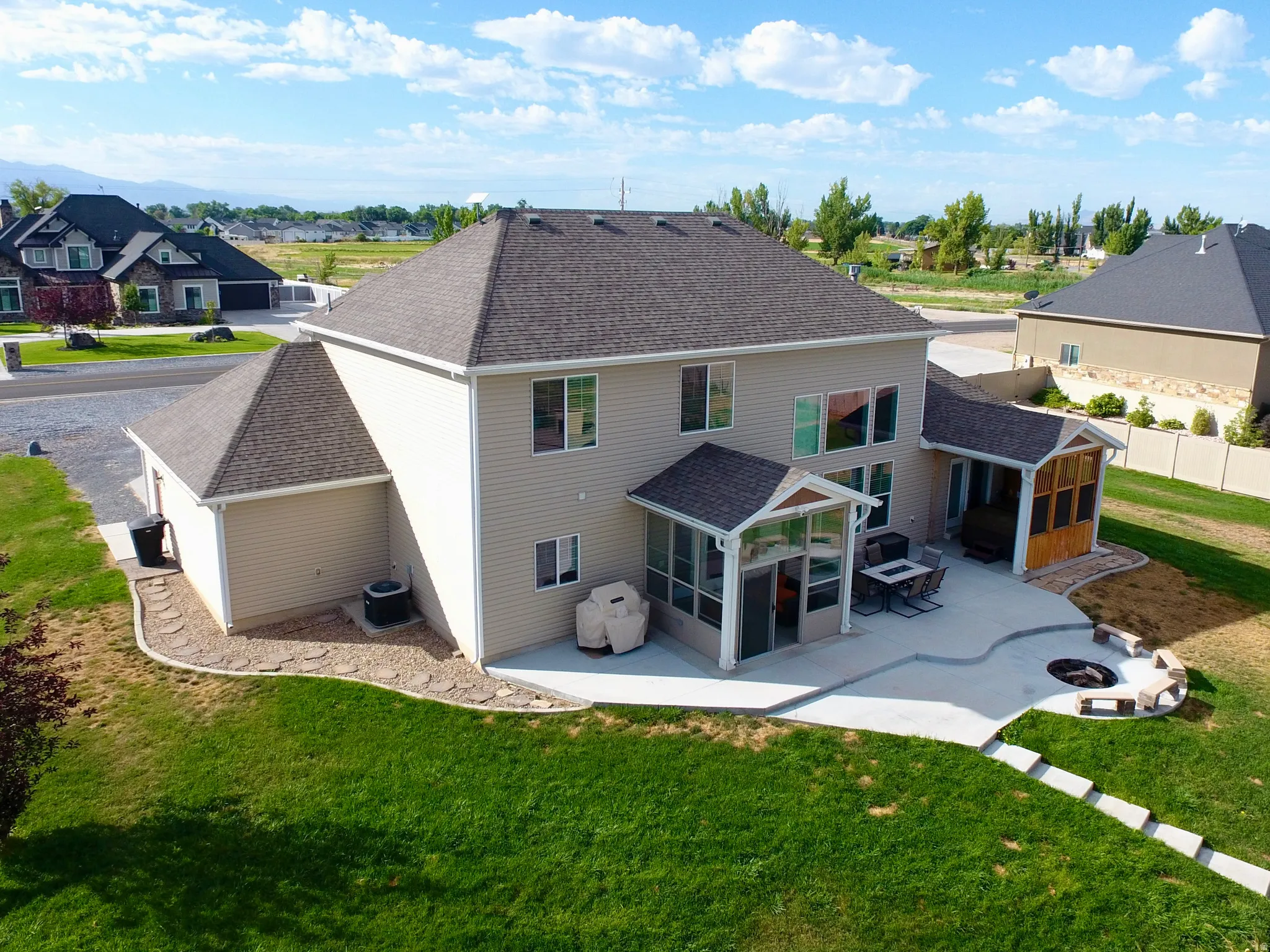 Rear exterior featuring a spacious concrete patio, screened-in porch, additional covered patio, built-in fire pit with stone seating, and a manicured lawn
