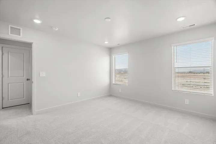 Recessed lighting, two windows with blinds, light-toned carpet, and a solid interior door