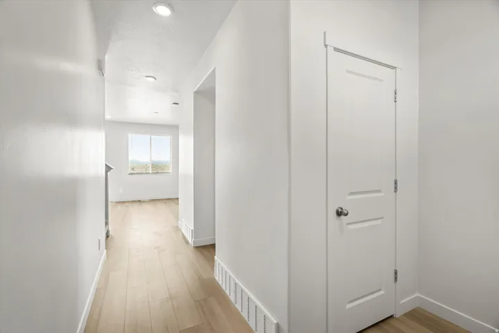 Hallway featuring wood-finish flooring, recessed lighting, white walls, and a paneled door