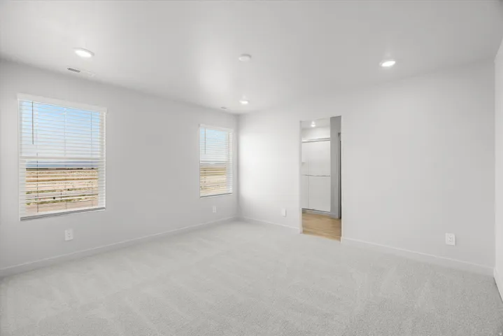 Bright and spacious bedroom featuring recessed ceiling lighting, carpet flooring, and multiple windows with horizontal blinds providing natural light