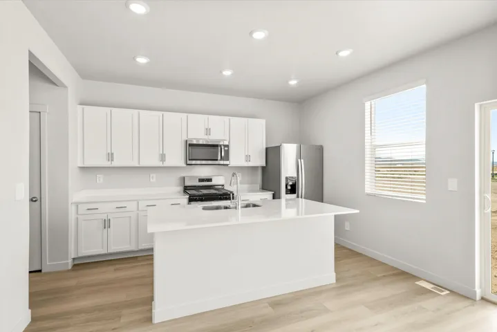 Modern kitchen featuring white cabinetry with stainless steel appliances, a large white island with waterfall-style countertop, recessed lighting throughout, and wood-finish flooring