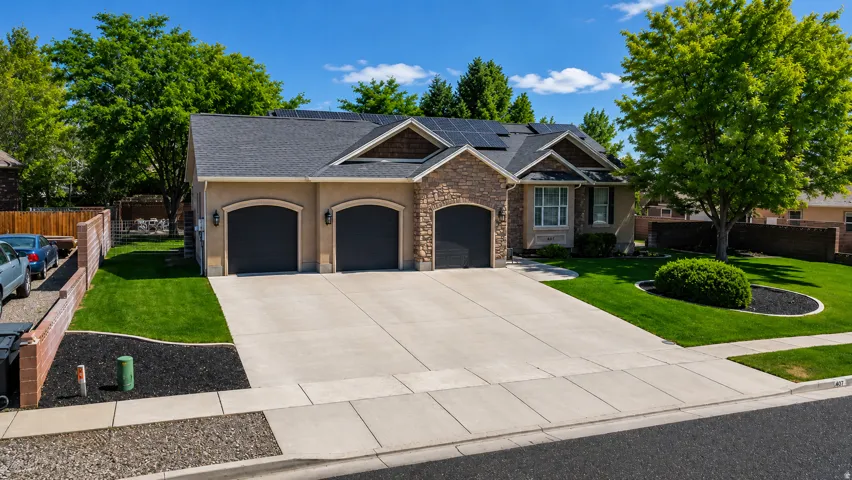 Exterior facade featuring a three-car garage, stone and stucco accents, and a prominent front yard with mature landscaping