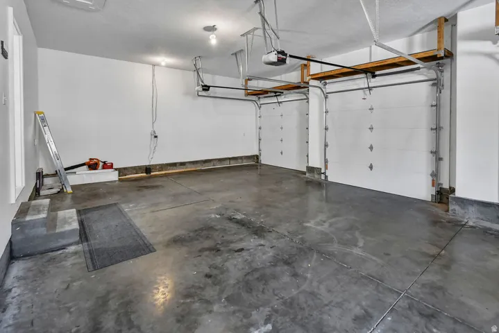 Two-car garage featuring automatic overhead doors, exposed ceiling joists, overhead lighting, and concrete flooring