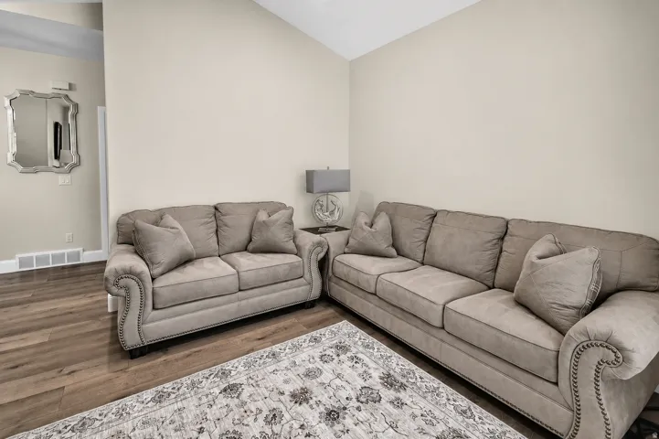 Spacious living area featuring wood-finish flooring, vaulted ceilings, and light-toned wall finishes