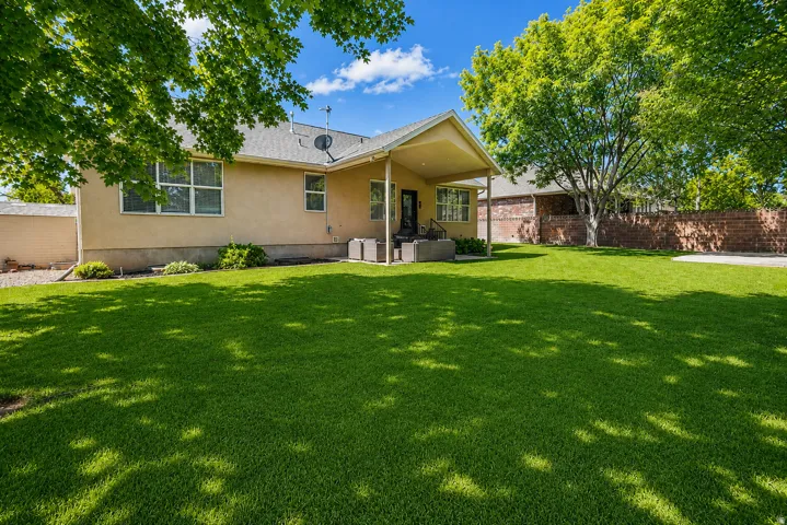 Spacious backyard featuring a lush lawn, mature trees providing natural shade, and a covered patio area with a concrete slab