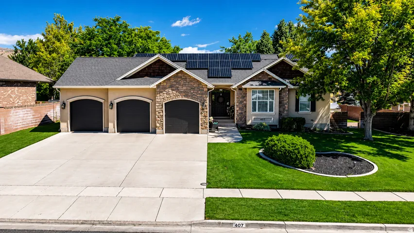 Stucco and stone facade with a multi-car driveway, a three-car garage, and a lush lawn