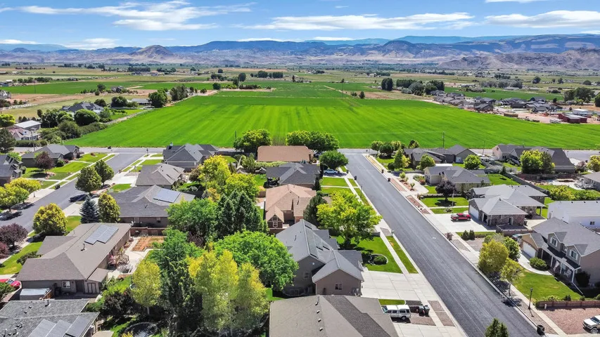 Expansive neighborhood featuring residential homes, mature landscaping, paved streets, and a backdrop of green fields and distant mountains