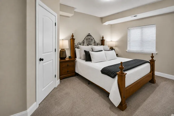 Carpeted room featuring a single window with blinds, neutral wall paint, and a white two-panel interior door with a black doorknob