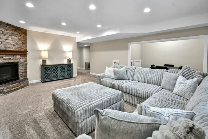 Finished living space featuring a stone-clad fireplace with a wood mantel, recessed lighting, carpeted flooring, and a cased opening to an additional area