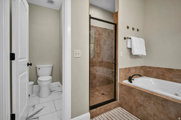 Bathroom featuring a built-in tub with bronze fixtures, a glass-enclosed shower with tiled walls, and a separate water closet with white tile flooring