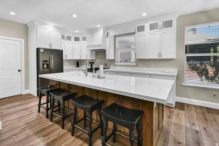 Kitchen featuring a large central island with seating, white shaker-style cabinetry, wood-finish flooring, and a stainless steel refrigerator