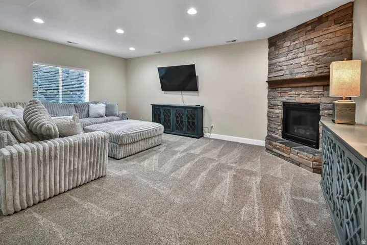 Spacious room featuring a stone-clad fireplace with a wood mantel, recessed lighting, neutral wall tones, and plush carpet flooring