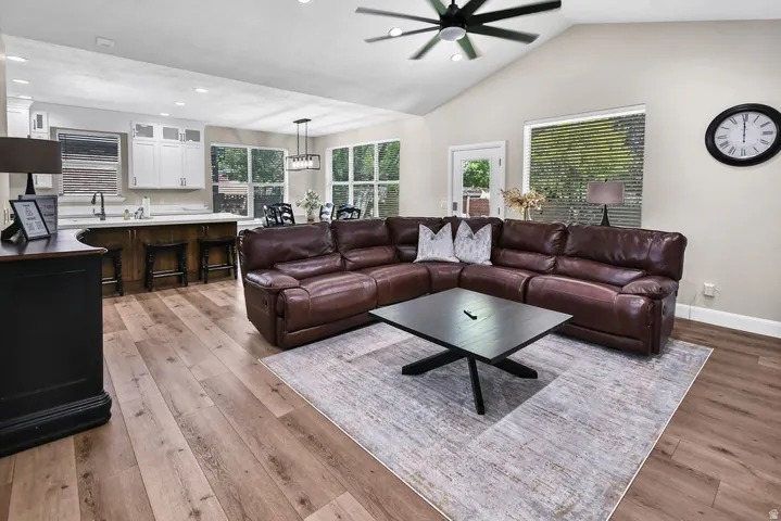 Vaulted ceiling living area with wood-finish flooring, a contemporary ceiling fan, and large windows