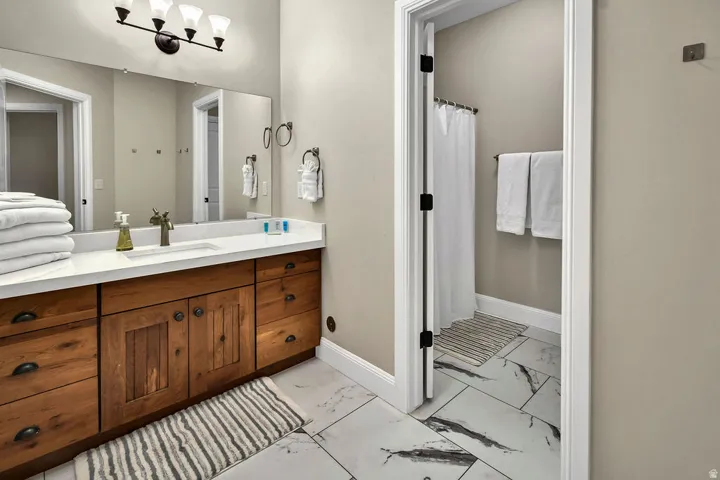 Bathroom featuring a long wood-finish vanity with a white countertop and integrated sink, under-mount cabinetry, and a large wall mirror