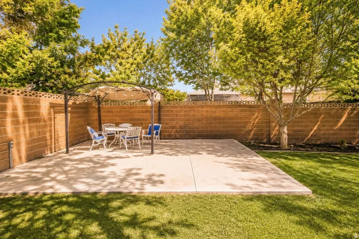 Expansive backyard featuring a concrete patio, a permanent metal gazebo structure, a block privacy wall, a manicured lawn, and mature trees