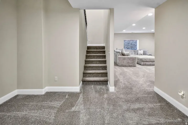 Carpeted staircase with dark handrail leading from a finished basement area featuring recessed lighting and a window