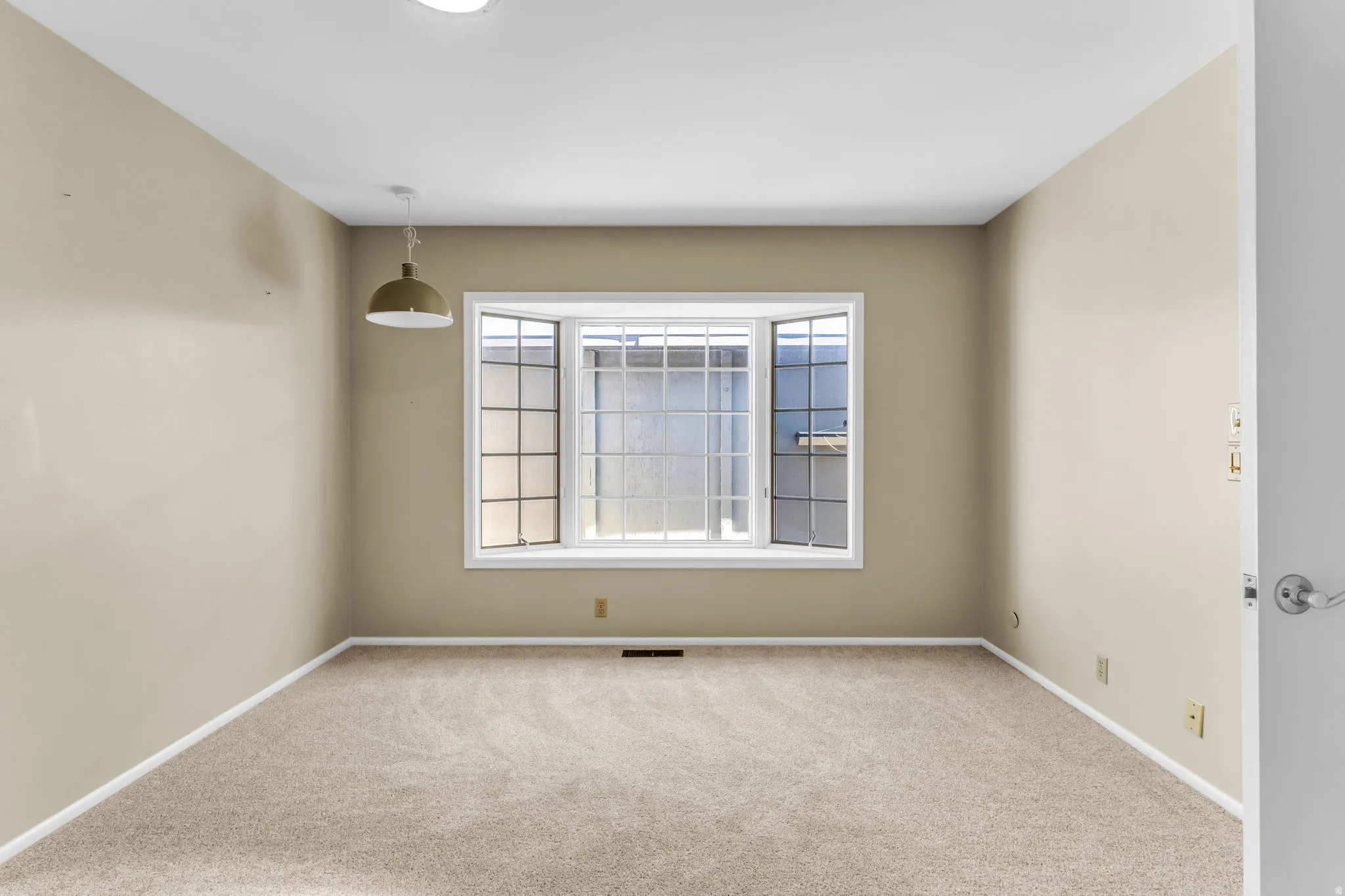 Neutral-toned interior featuring a bay window with multiple panes, recessed ceiling lighting, a suspended pendant light fixture, light-colored carpeting, and white baseboards