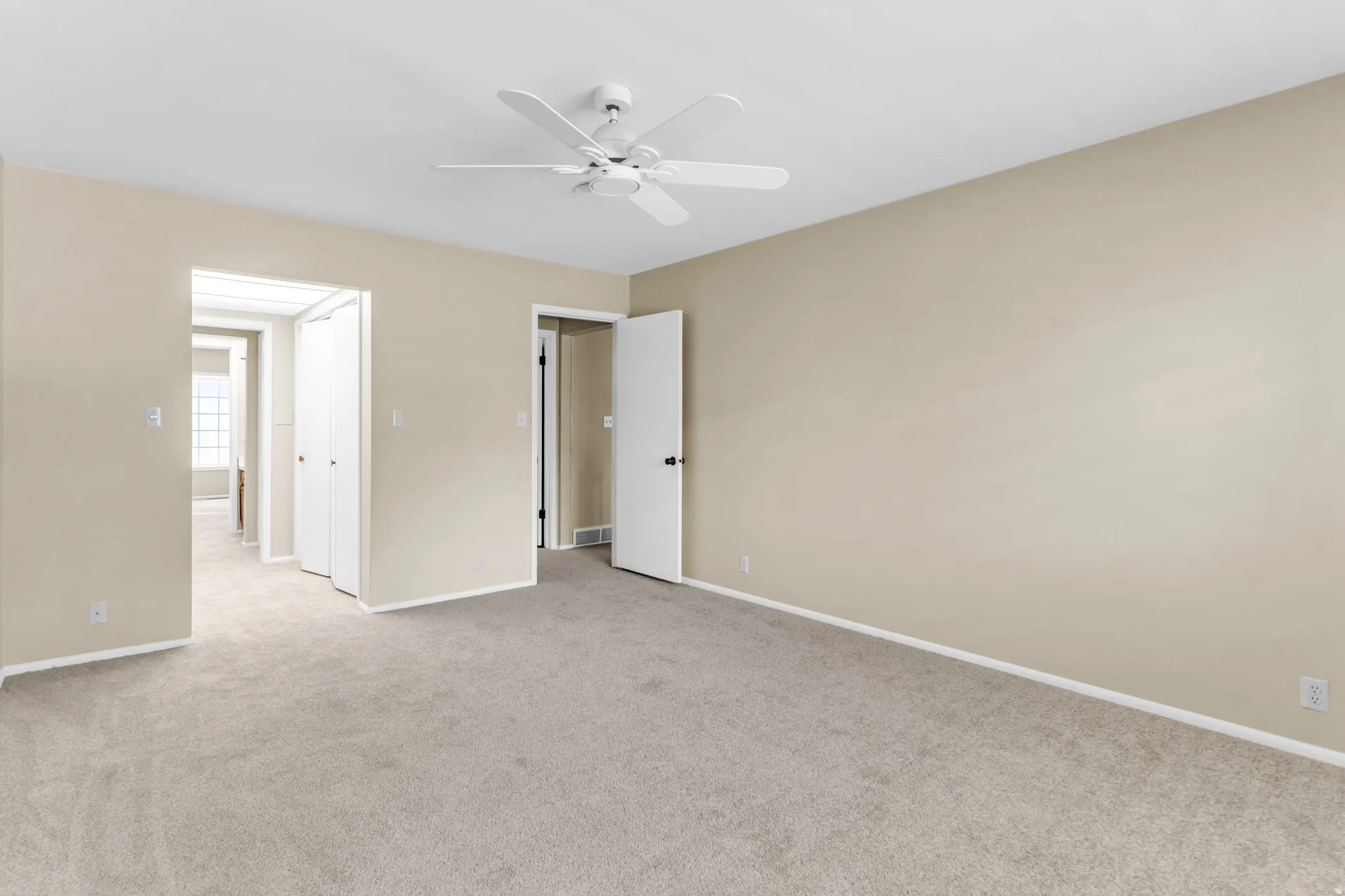 Spacious room with neutral-toned walls, light-colored carpet, and a ceiling fan