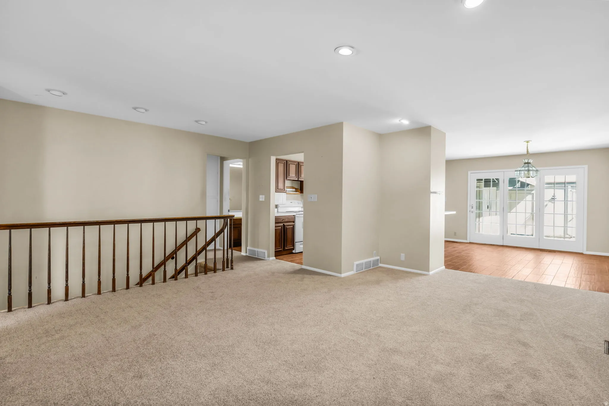 Carpeted living area featuring recessed lighting, a wood baluster railing, and neutral wall tones