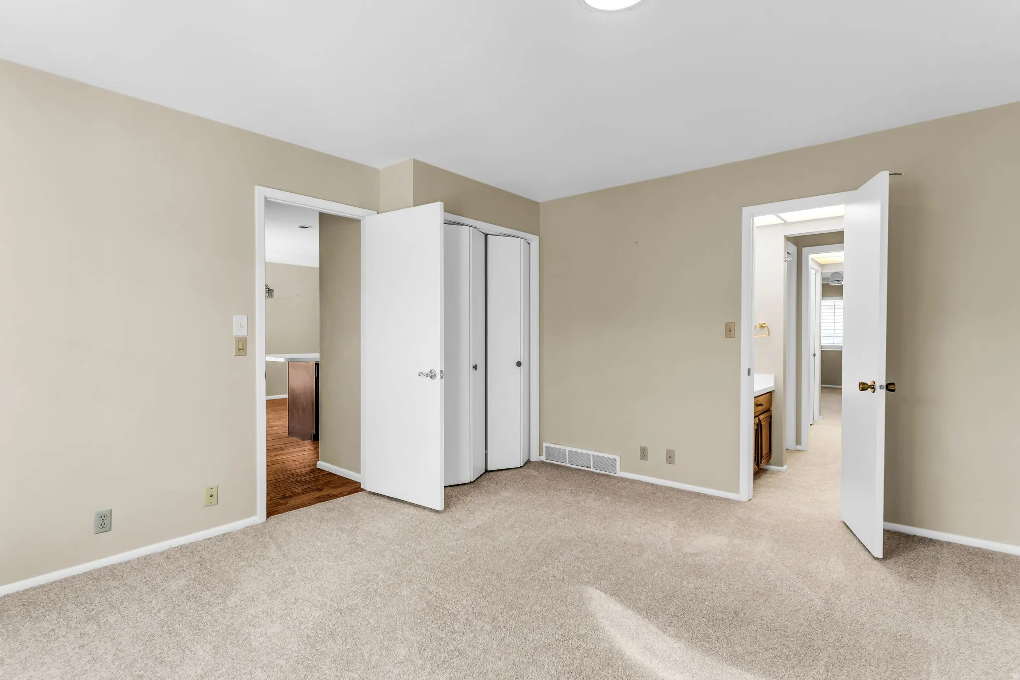 Neutral-toned carpeted room featuring a ceiling light fixture, white baseboards, and two doorways with white trim