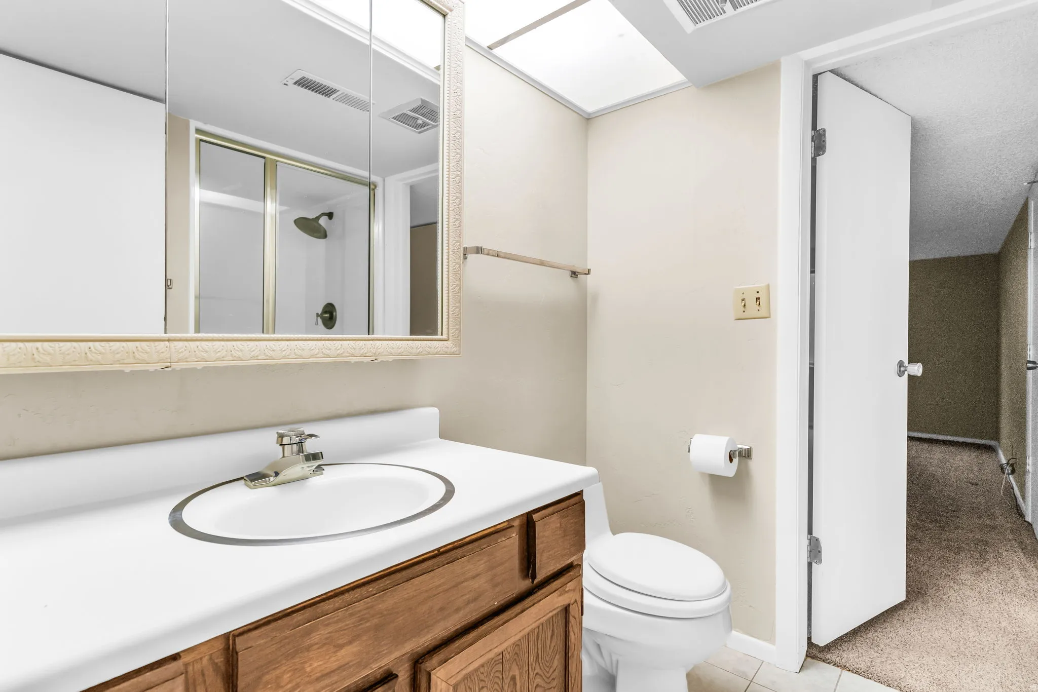 Bathroom featuring a wood-finish vanity with an integrated sink, a mirrored medicine cabinet, a toilet, a shower with a sliding glass door, and overhead lighting