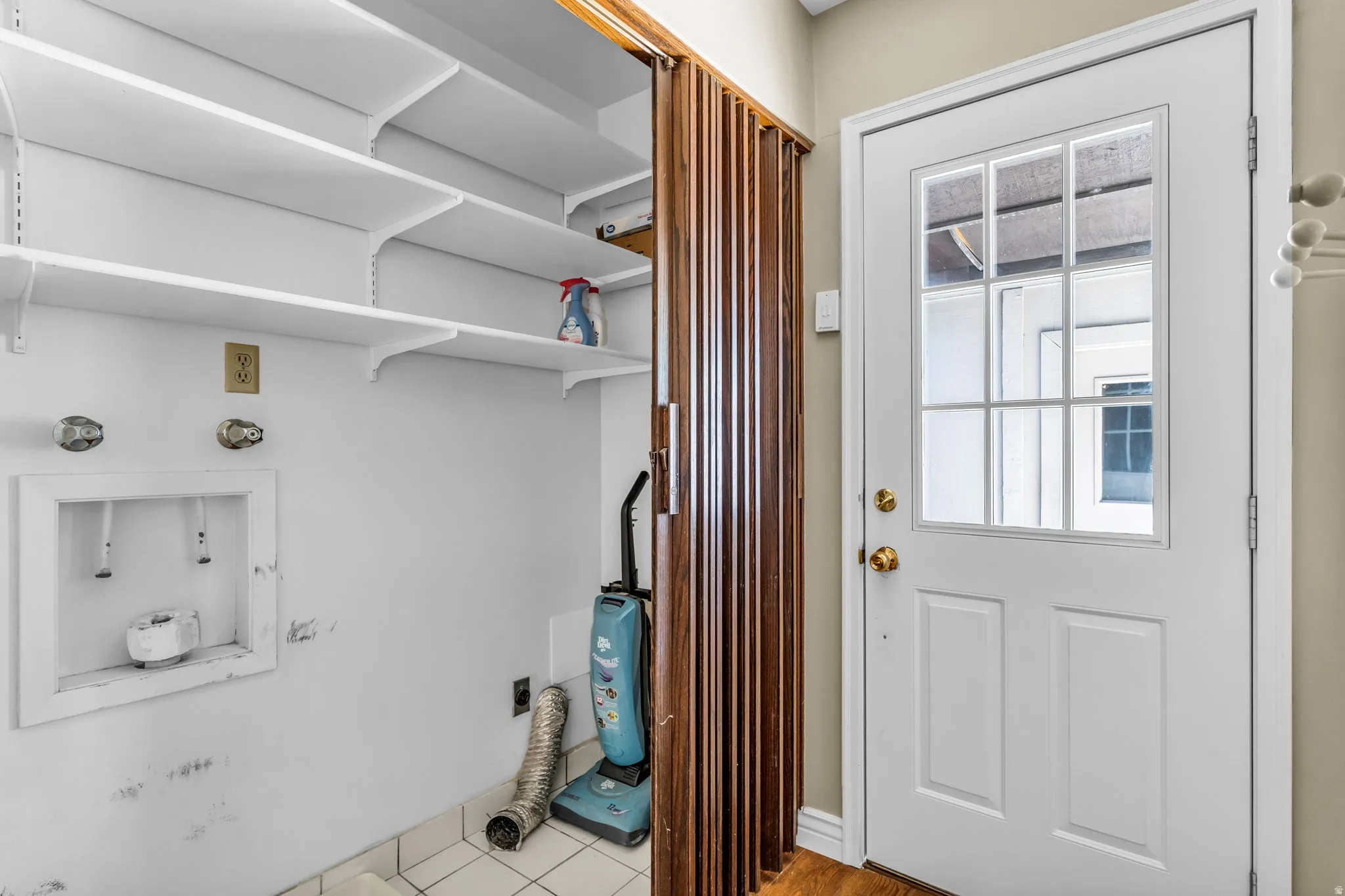 Laundry area featuring adjustable white shelving, water hookups, and a white paneled door with a multi-pane glass insert
