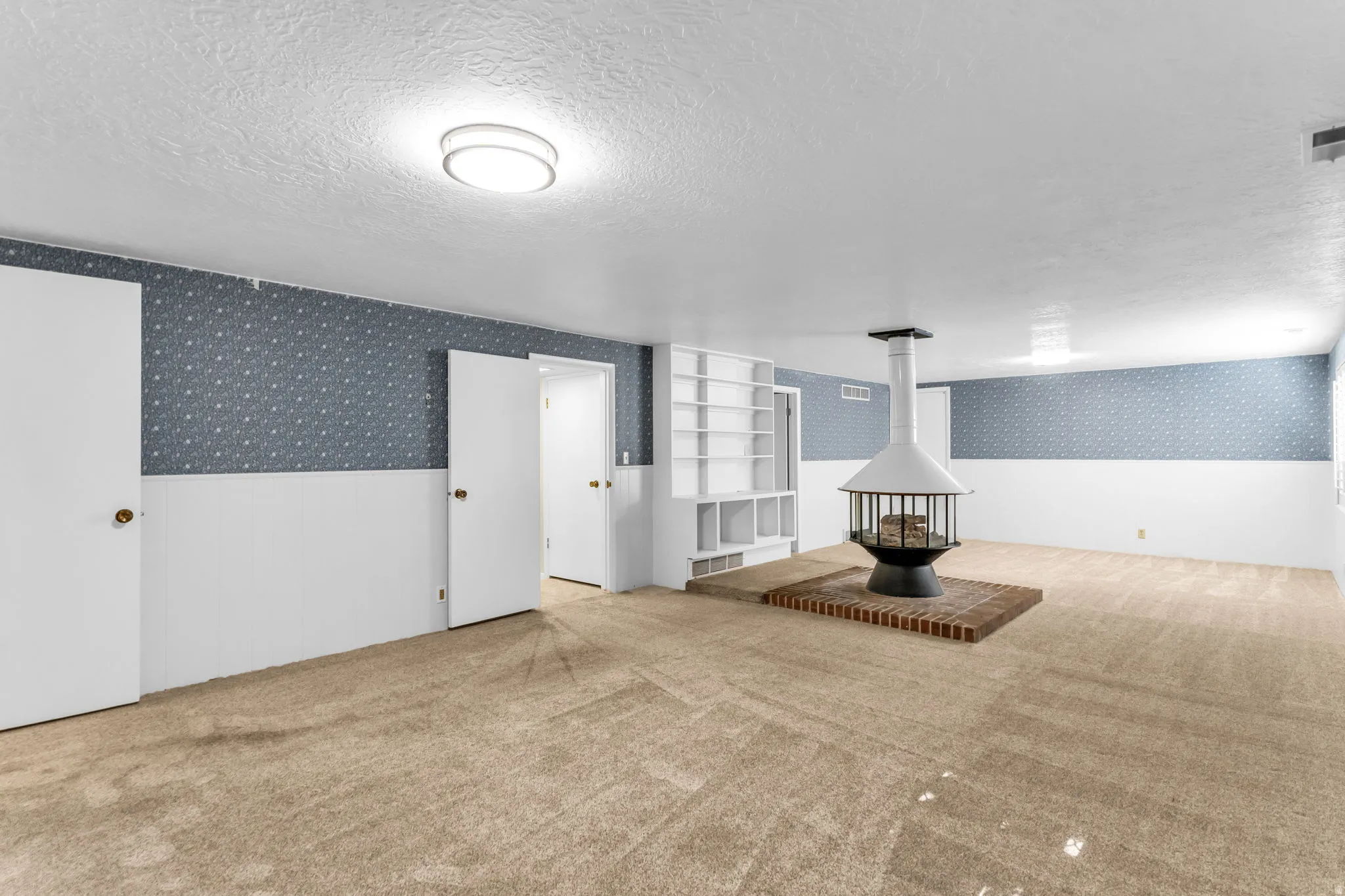 Spacious room featuring a central freestanding fireplace on a brick hearth, built-in shelving, and light-colored carpeting