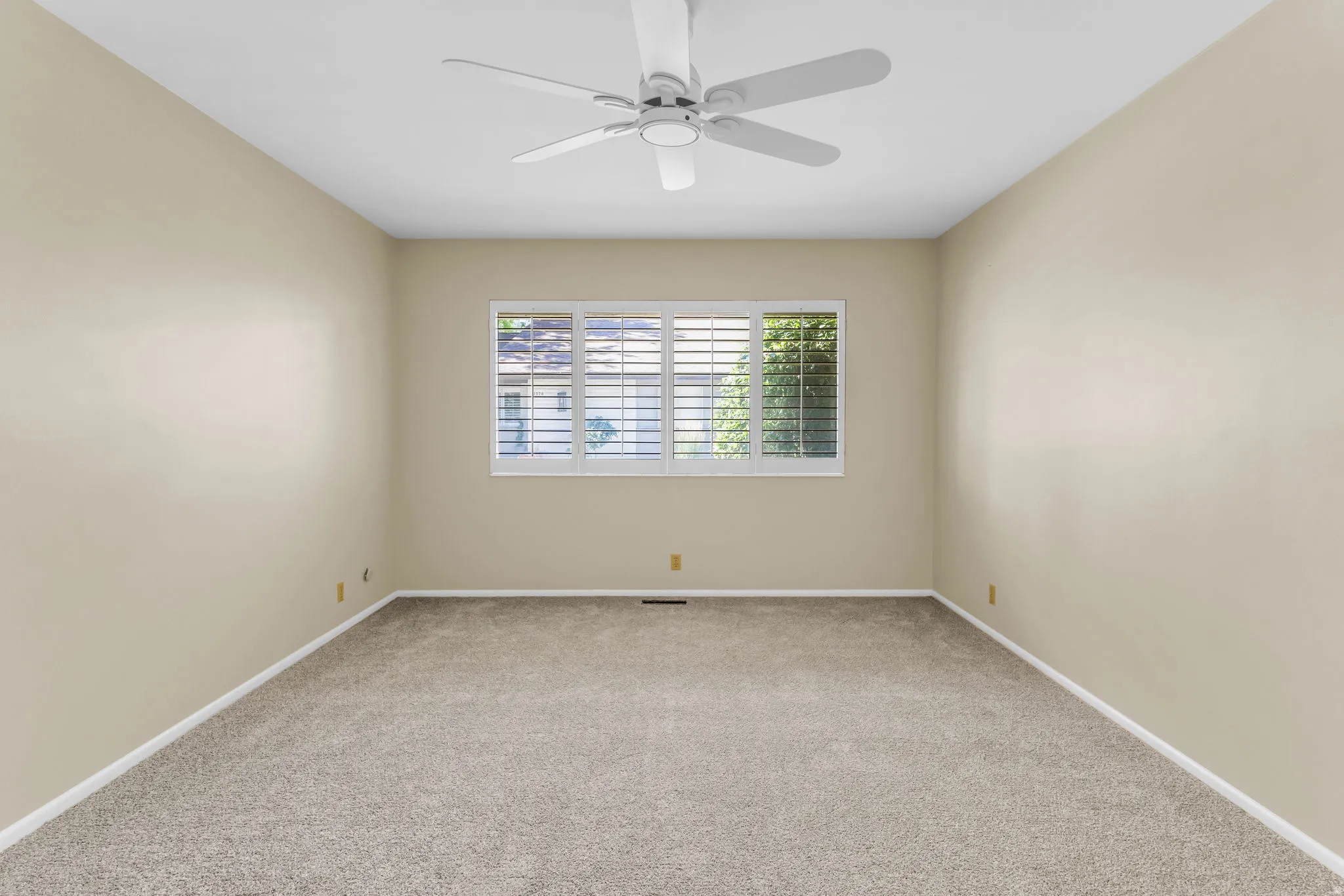 Neutral-toned room featuring a white ceiling fan, light beige walls, and carpet flooring