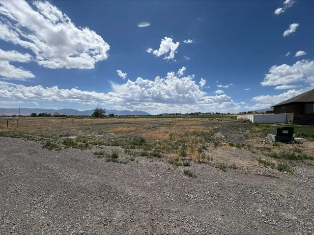 Expansive land parcel featuring a gravel surface, partial fencing, distant mountain ranges, and a clear sky