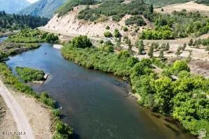 Winding river with green banks, bordered by a dirt road and distant mountains