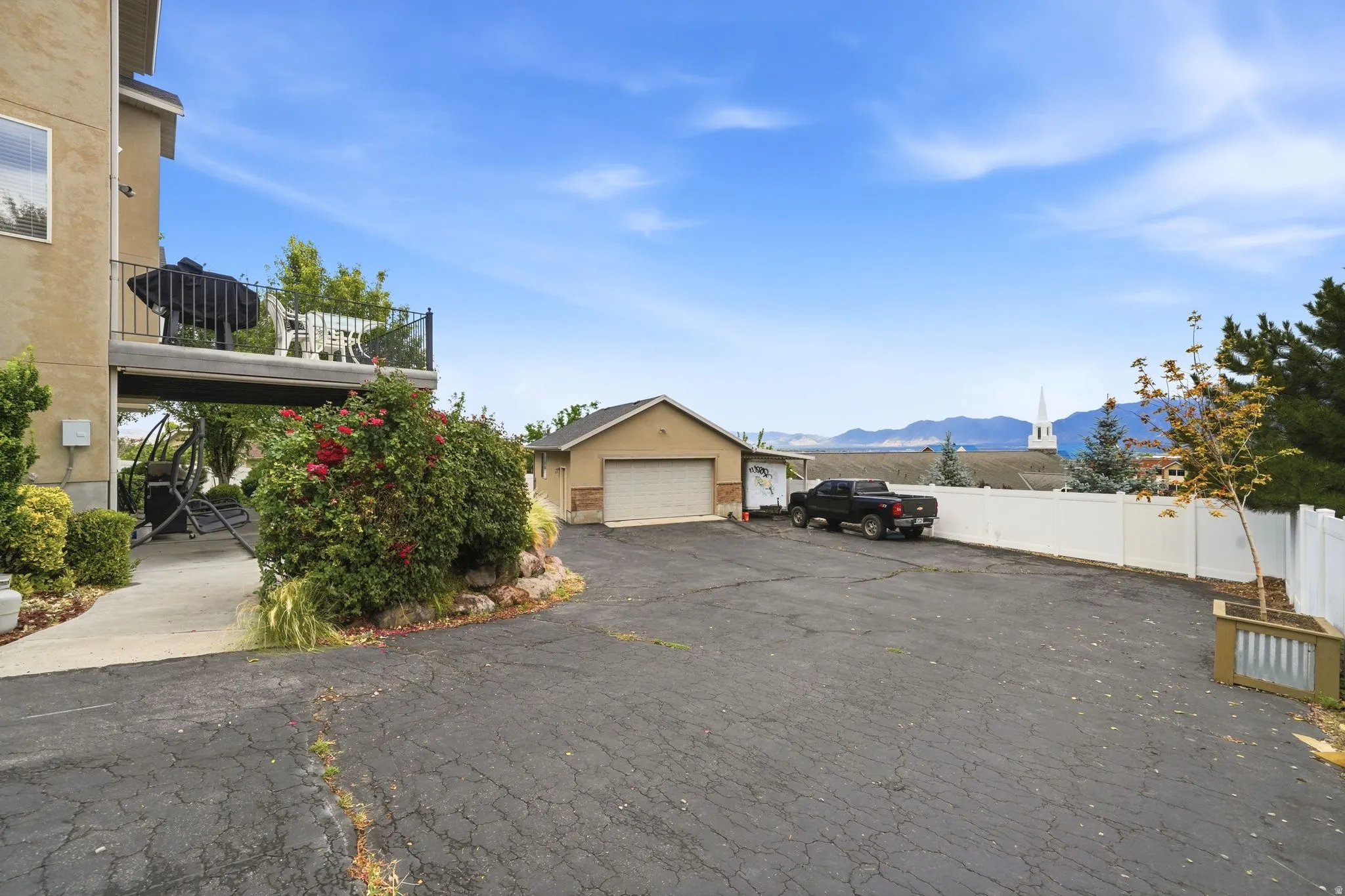 Expansive paved driveway and detached garage, complemented by mature landscaping and a white privacy fence