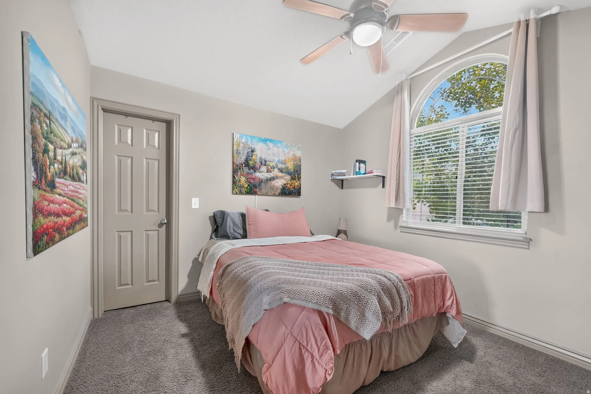 Vaulted ceiling room featuring an arched window with blinds, a ceiling fan with light fixture, gray plush carpet, and a six-panel interior door