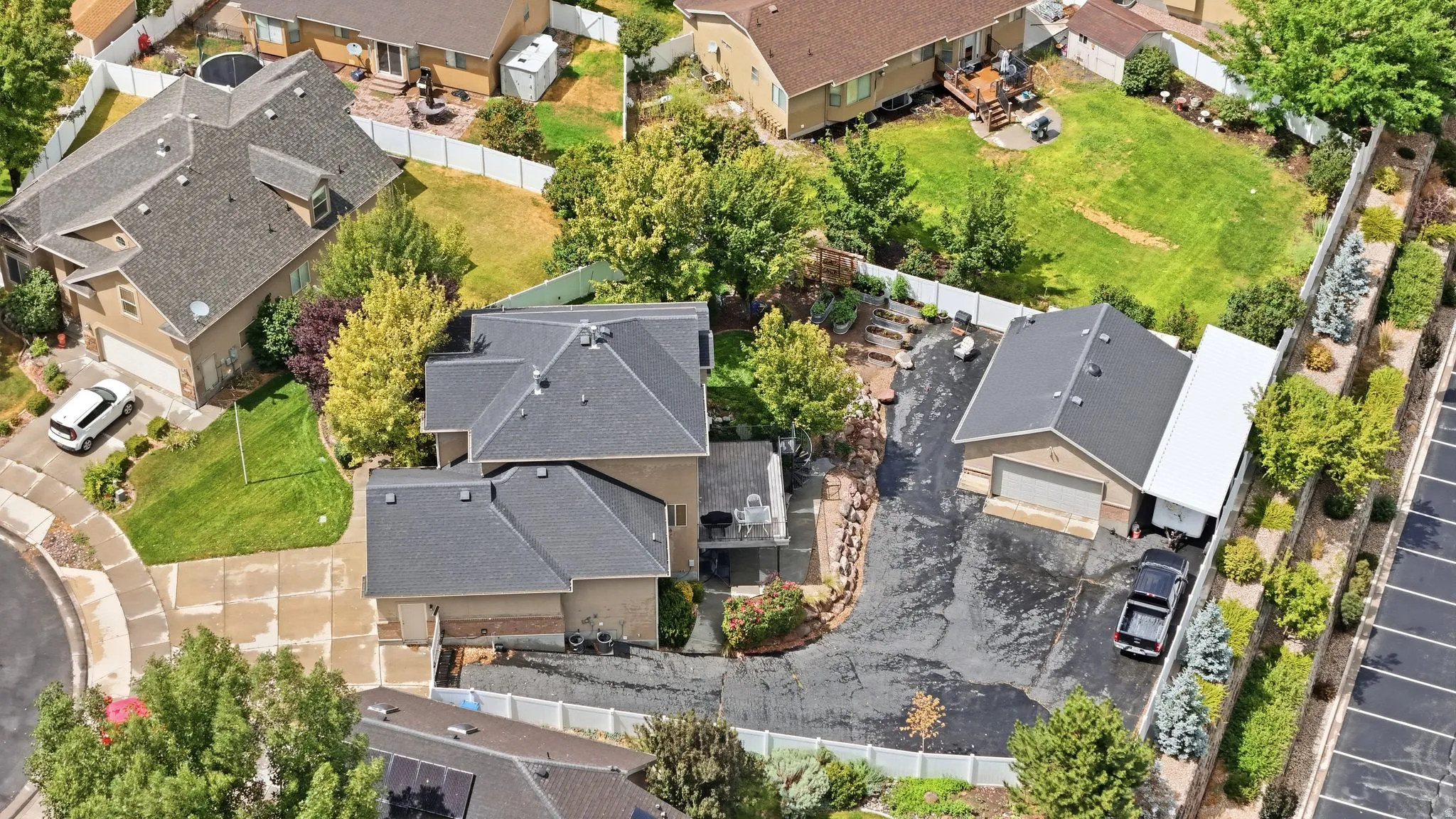 Expansive property featuring a multi-level residence with a gray shingle roof, a detached garage with an extended covered area, and a large paved driveway