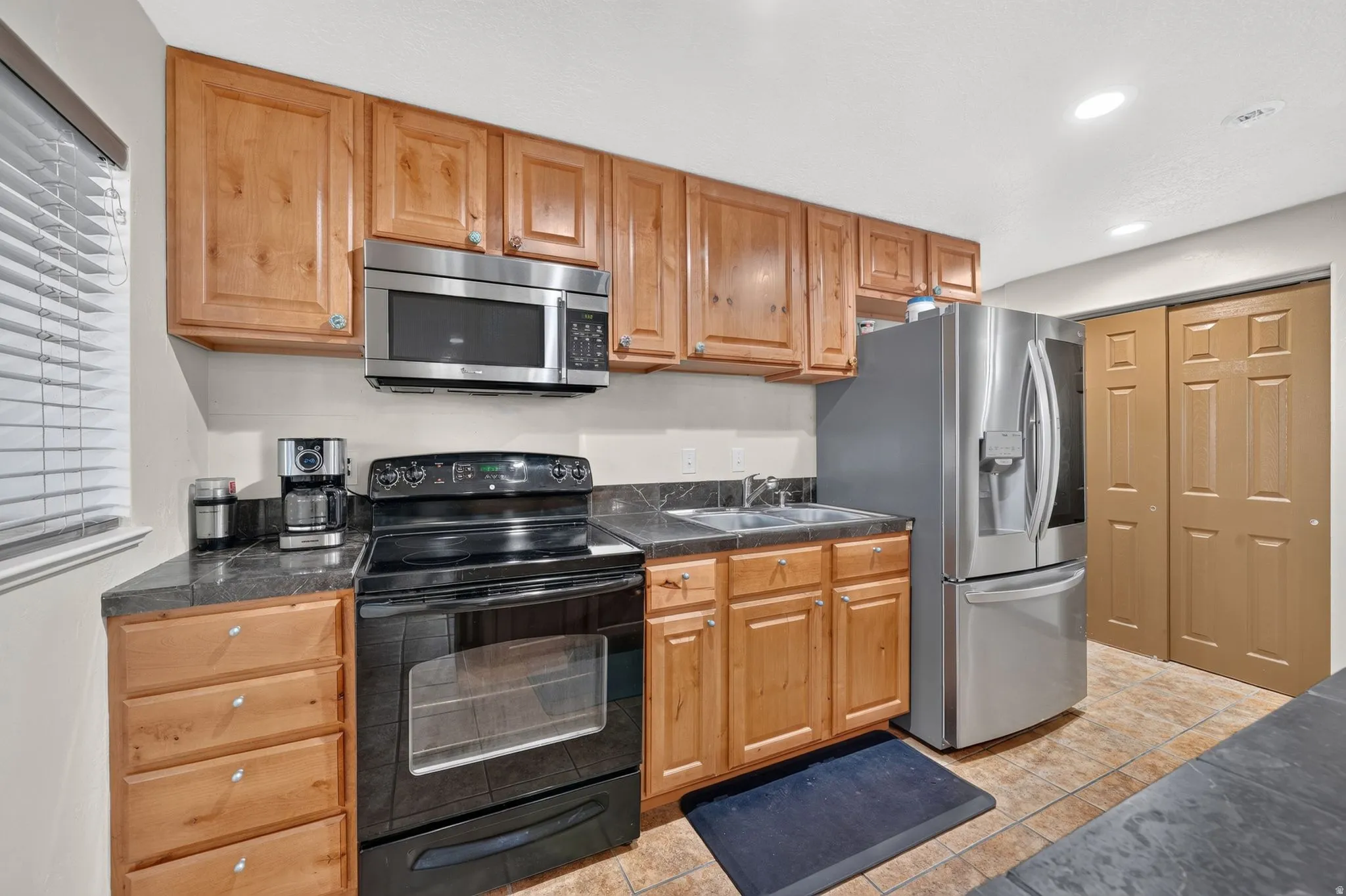 Kitchen featuring wood-finish cabinetry, stainless steel appliances, dark countertops, and tile flooring