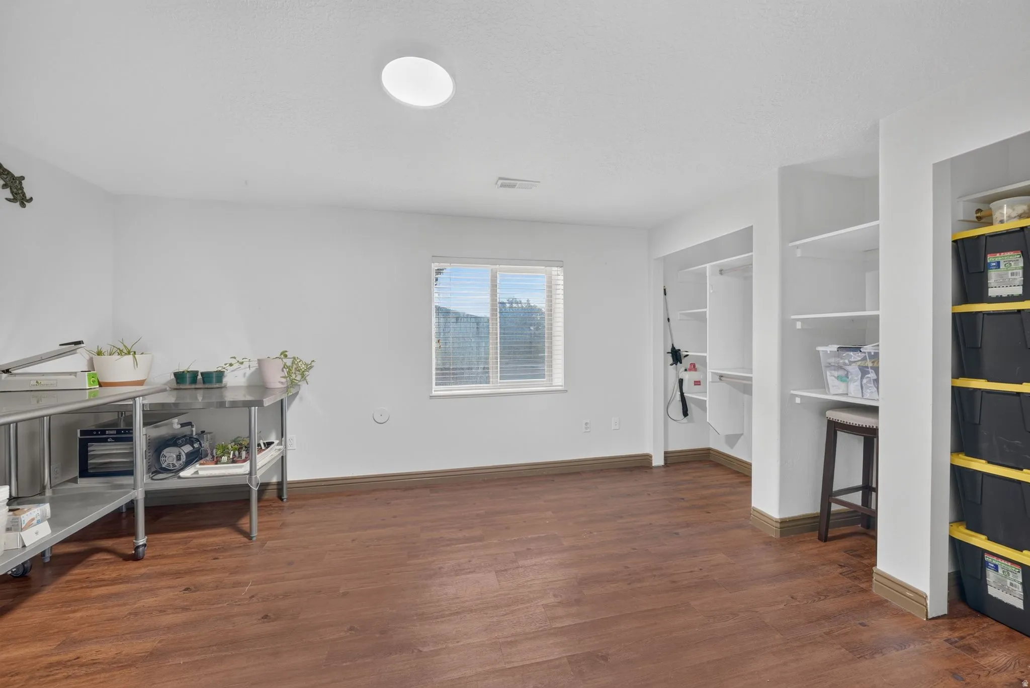 Brightly lit interior space featuring wood-finish flooring, a window with blinds, and recessed shelving for storage