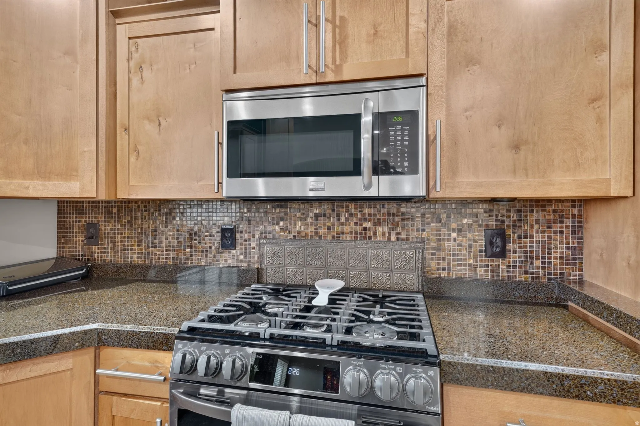 Stainless steel gas range and built-in microwave, complemented by wood cabinetry and a mosaic tile backsplash
