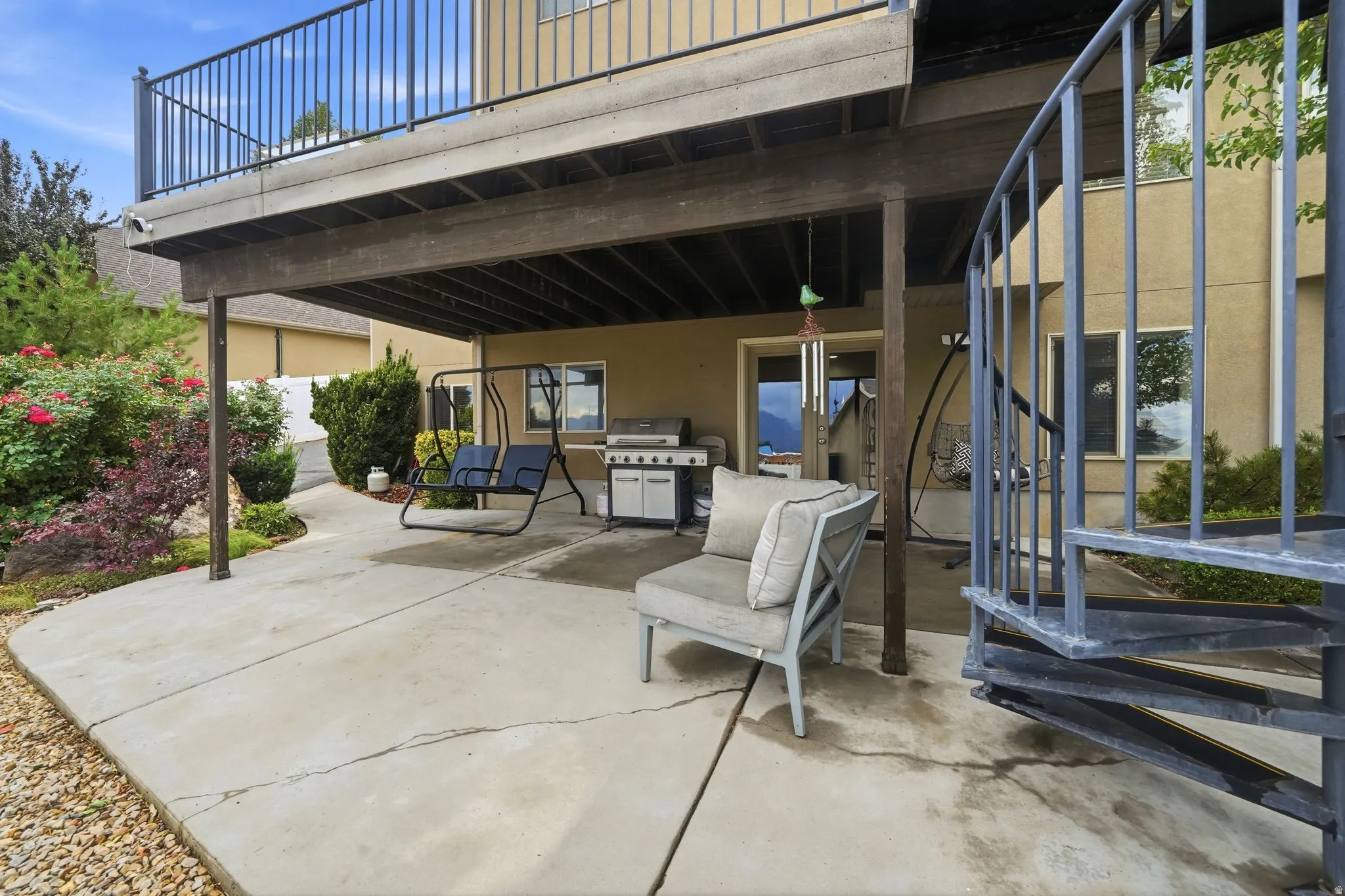 Spacious concrete patio featuring an overhead deck, metal spiral staircase, and a cultivated garden bed