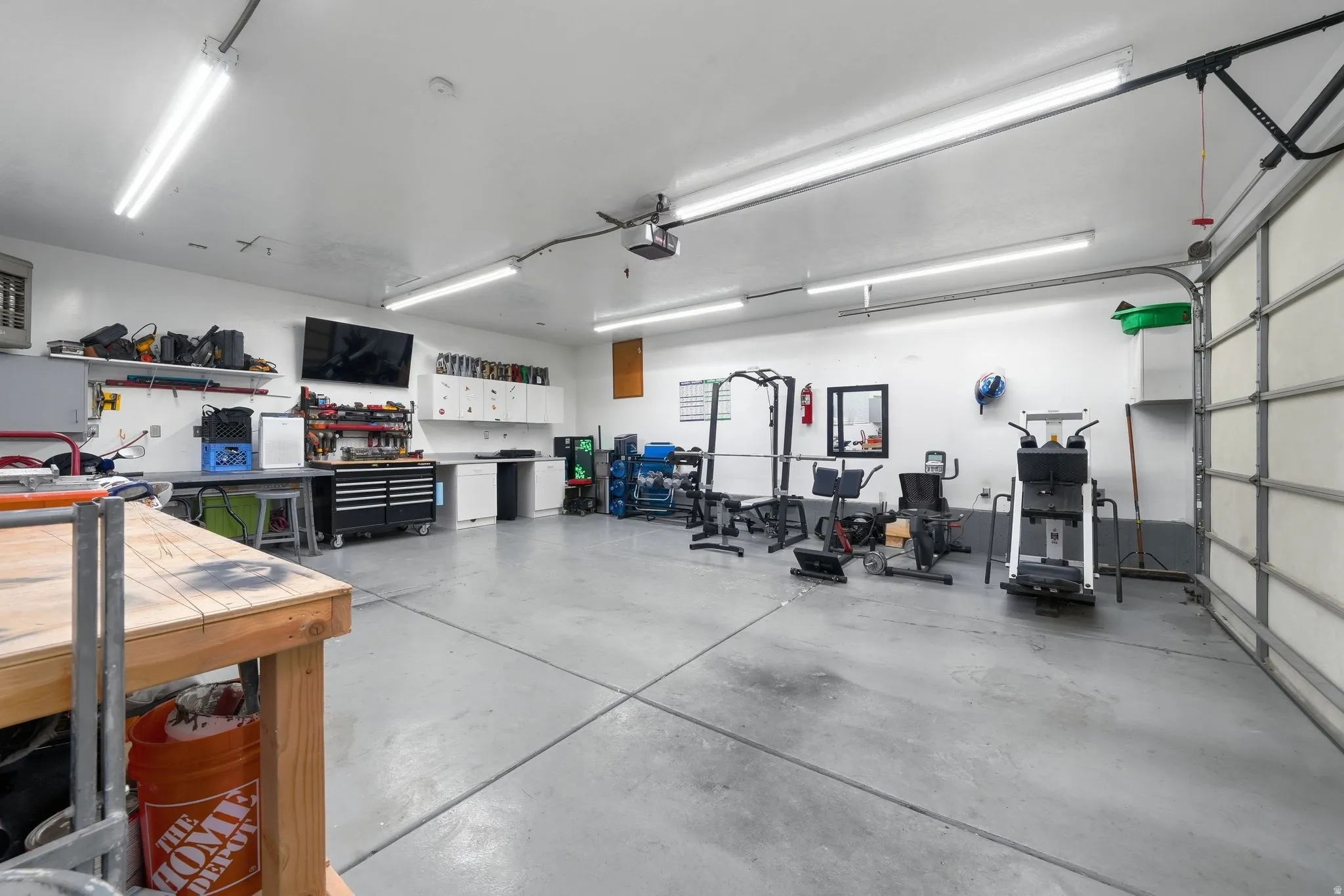 Spacious garage featuring a concrete floor, multiple fluorescent light fixtures, overhead garage door with track system, built-in shelving, and white cabinetry