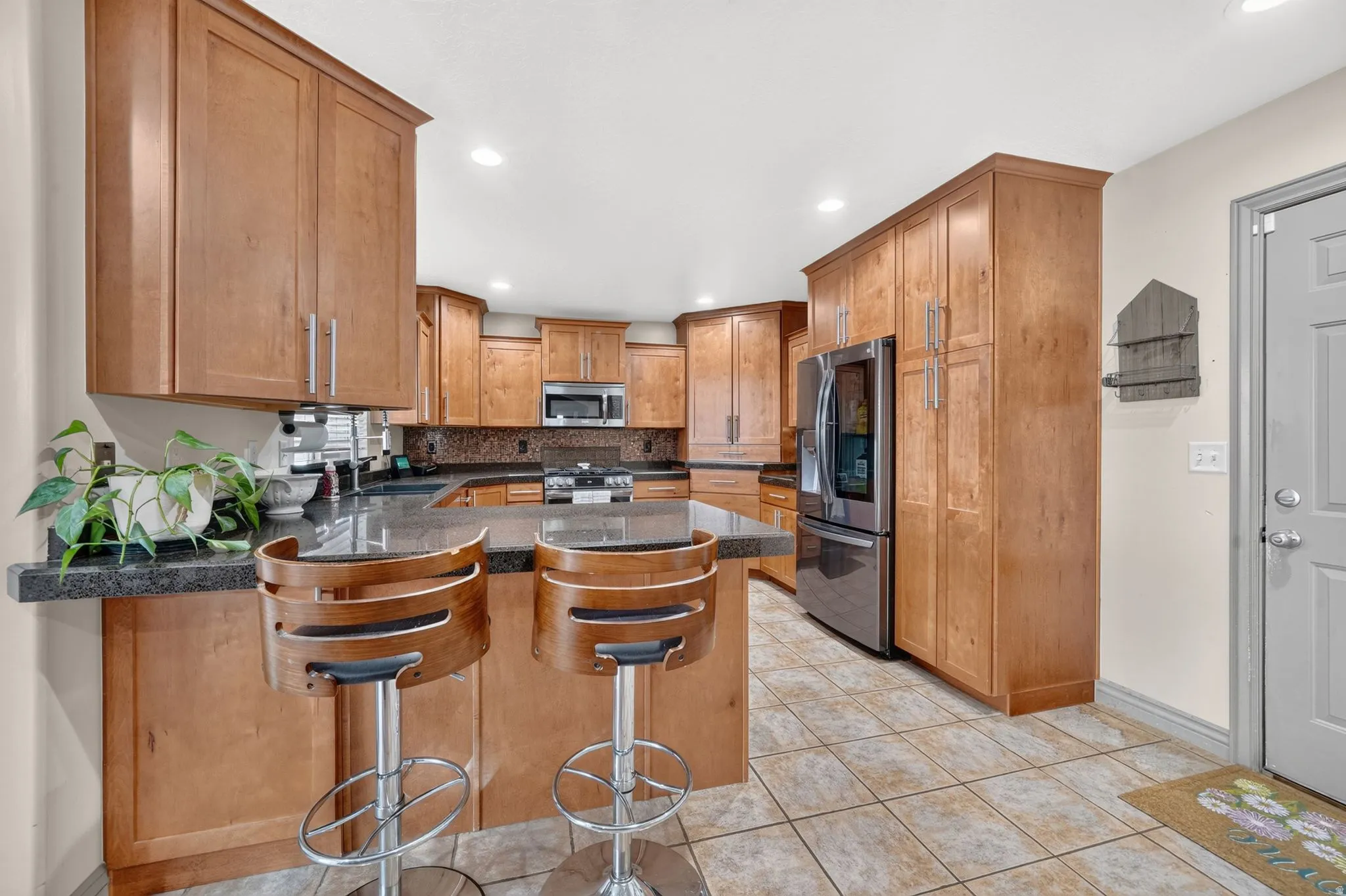 Kitchen featuring a breakfast bar with dark countertops, extensive wood cabinetry, stainless steel appliances, and tiled flooring