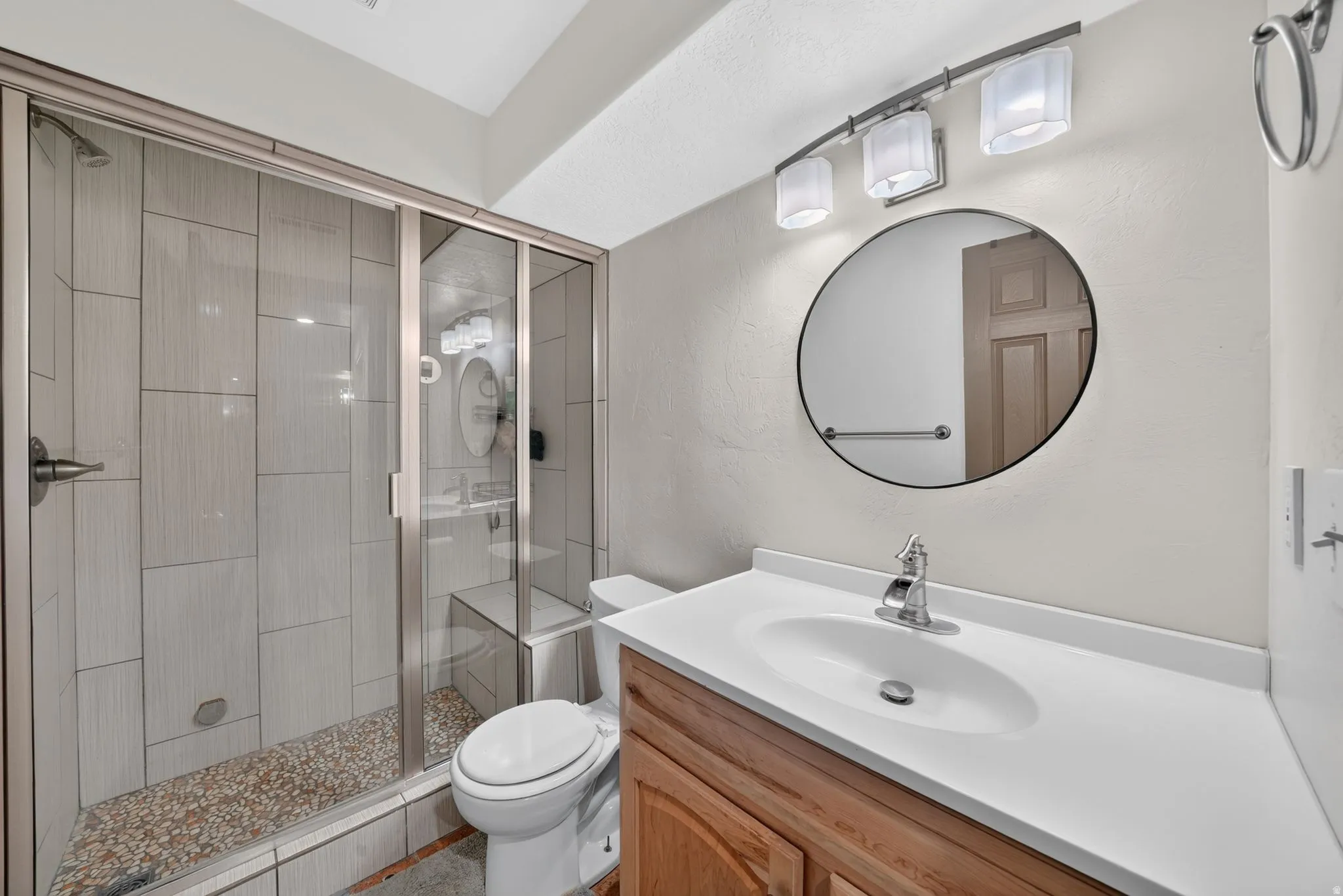 Bathroom featuring a glass-enclosed shower with pebble-style flooring and light-toned wall tiling