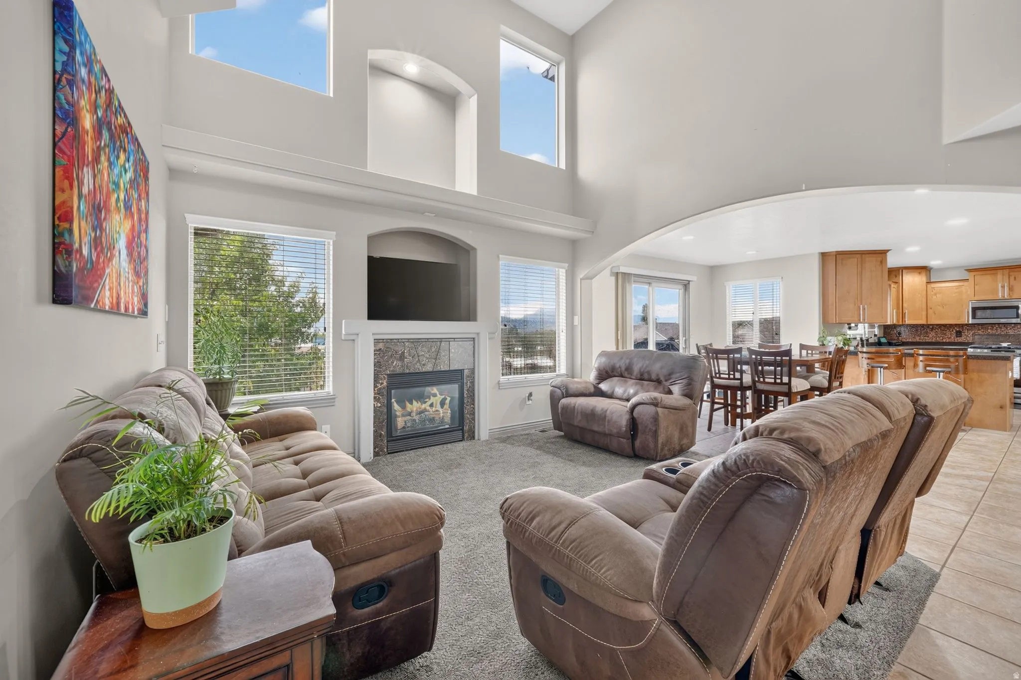 Spacious living area featuring high ceilings, a stone fireplace, and multiple windows providing natural light